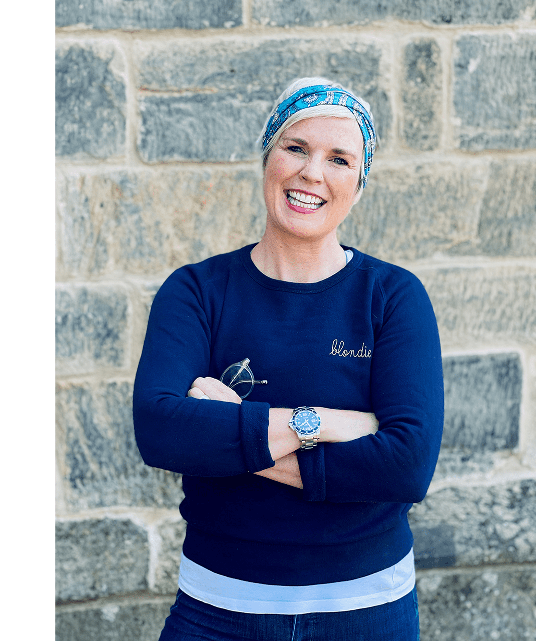 Dani Carlaw stands cheerfully in front of the camera with her arms crossed in front of her, wearing a bright light blue headband and a navy blue sweater