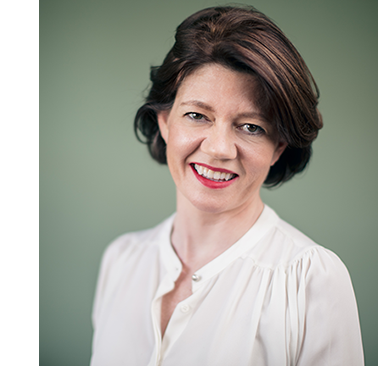 Isabel Davis stands wearing a white shirt against a sage green background