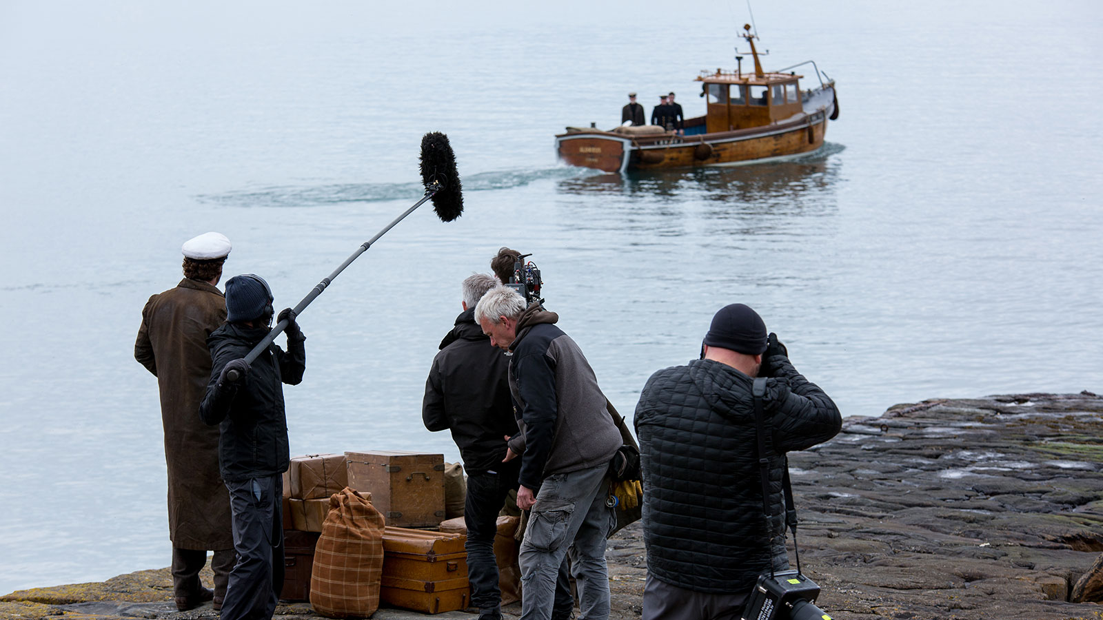 A filmcrew are filming a scene where a boat is driving off in the distance