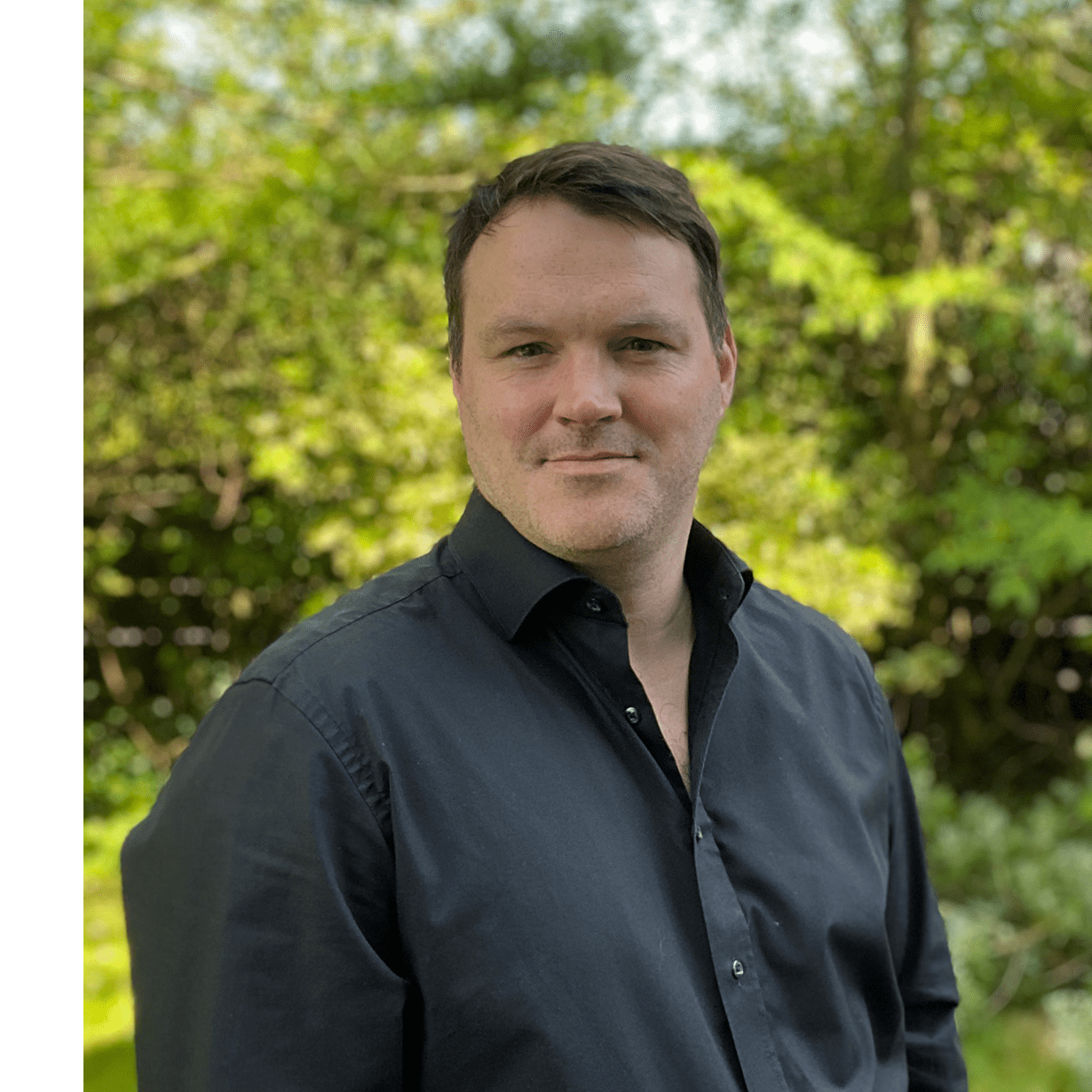 Kieran Hannigan wears a dark shirt in front of a leafy green background