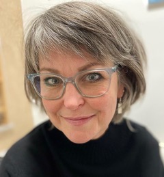 A close up headshot of Fi who has short hair and wears glasses - she is looking up at the camera slightly