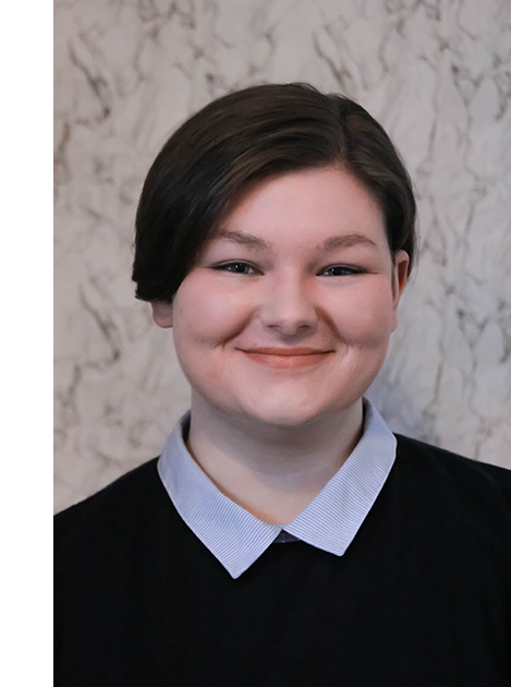 Meghan smiles at the camera, wearing a jumper over a shirt