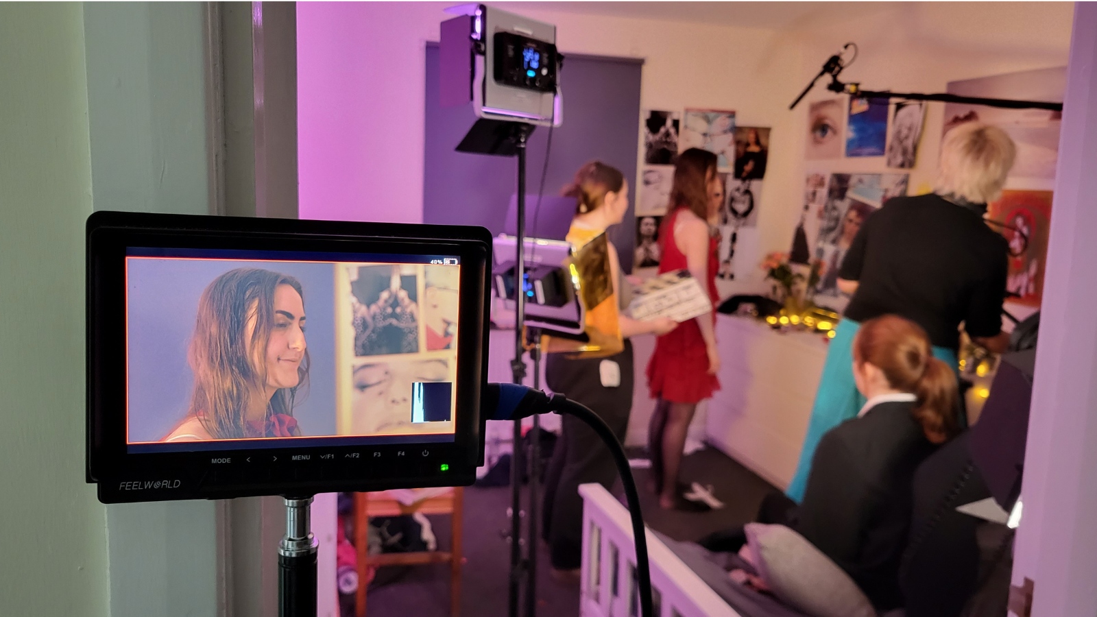 On the left is a monitor showing a close of a girl's face, behind this is. the set where filming is. taking place. three other people are in the room assisting with filming