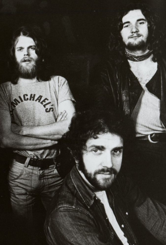 Black and white image of three members of the Scottish band, Average White Band, who sit in two rows smiling at the camera