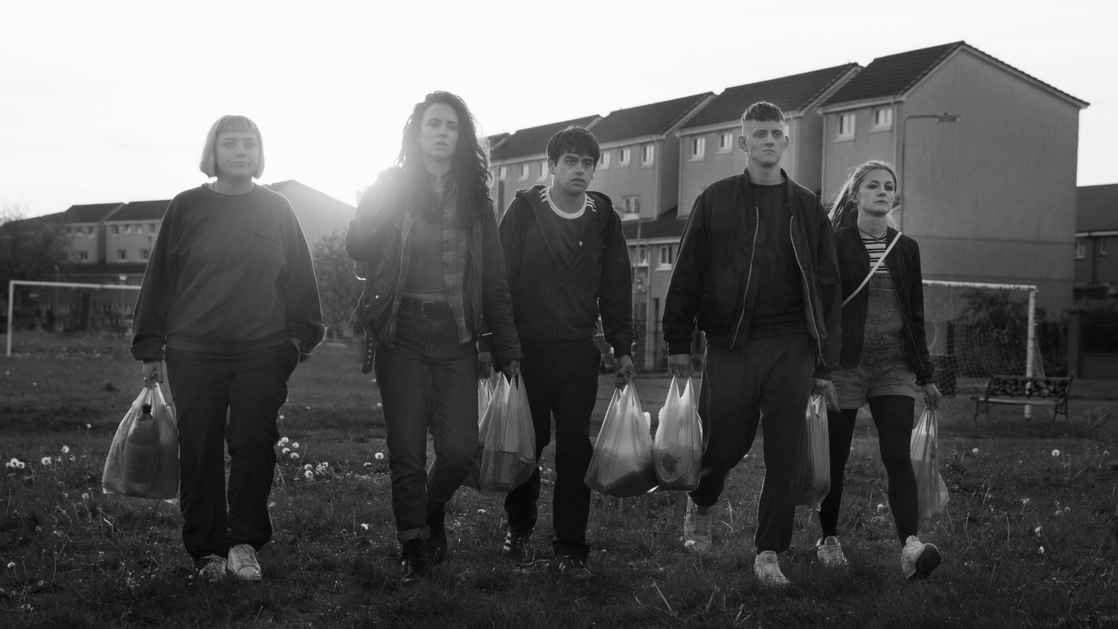 A group of teenagers walk through a grassy field holding plastic bags