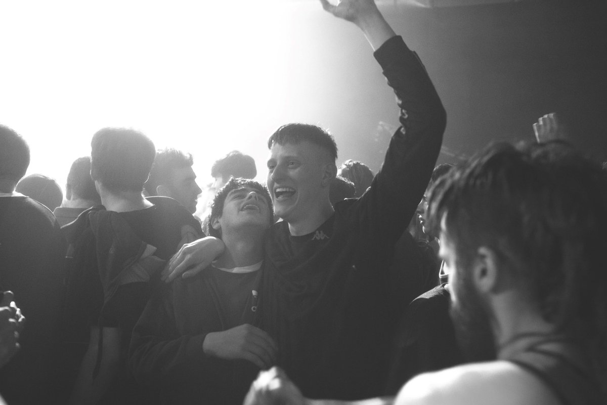 Black and white image of two men in night club with arms around each other