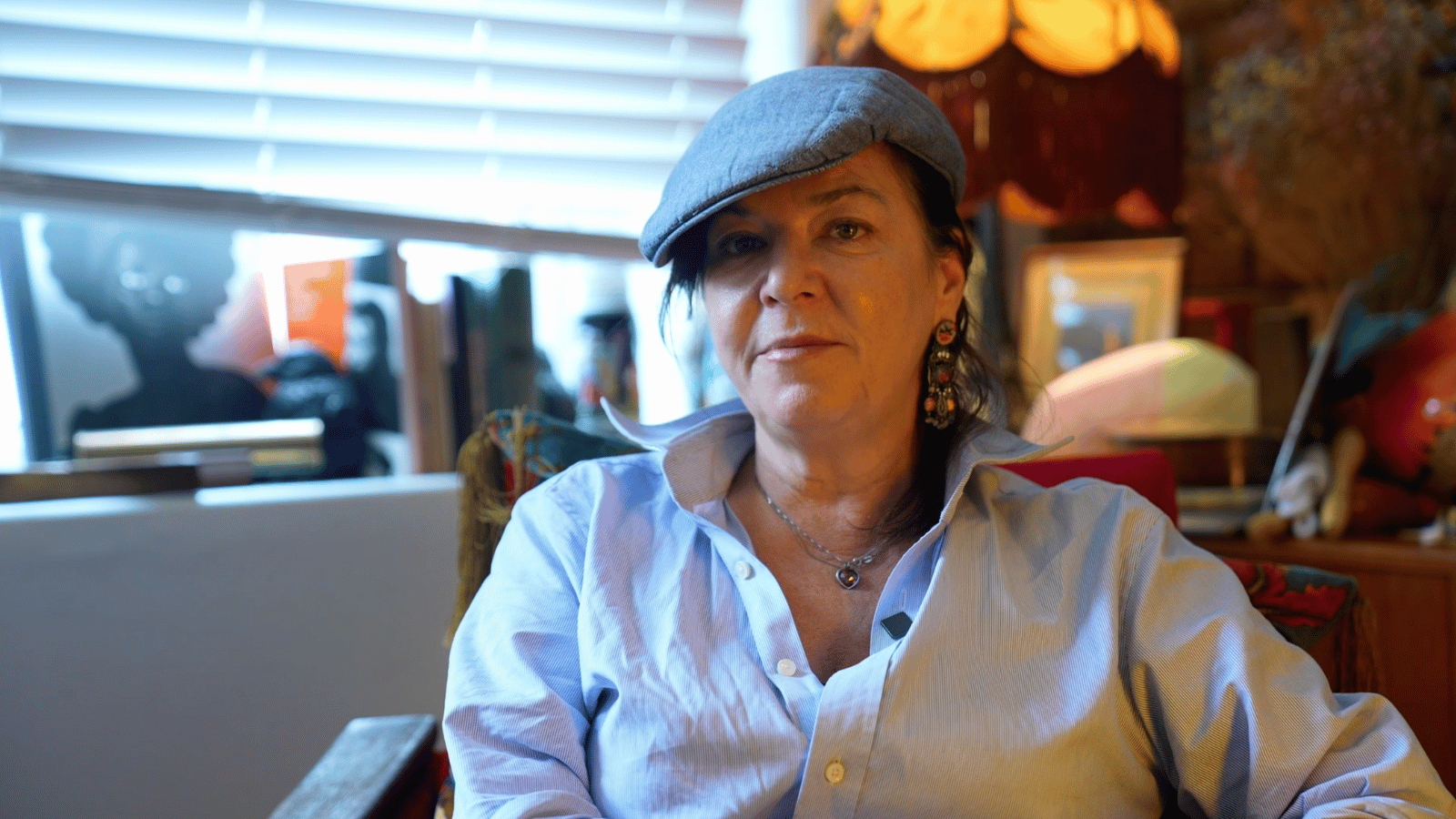 Still from Bill Douglas: My Best Friend. Filmmaker Lynn Ramsey sitting on chair looking at the camera in a living room.