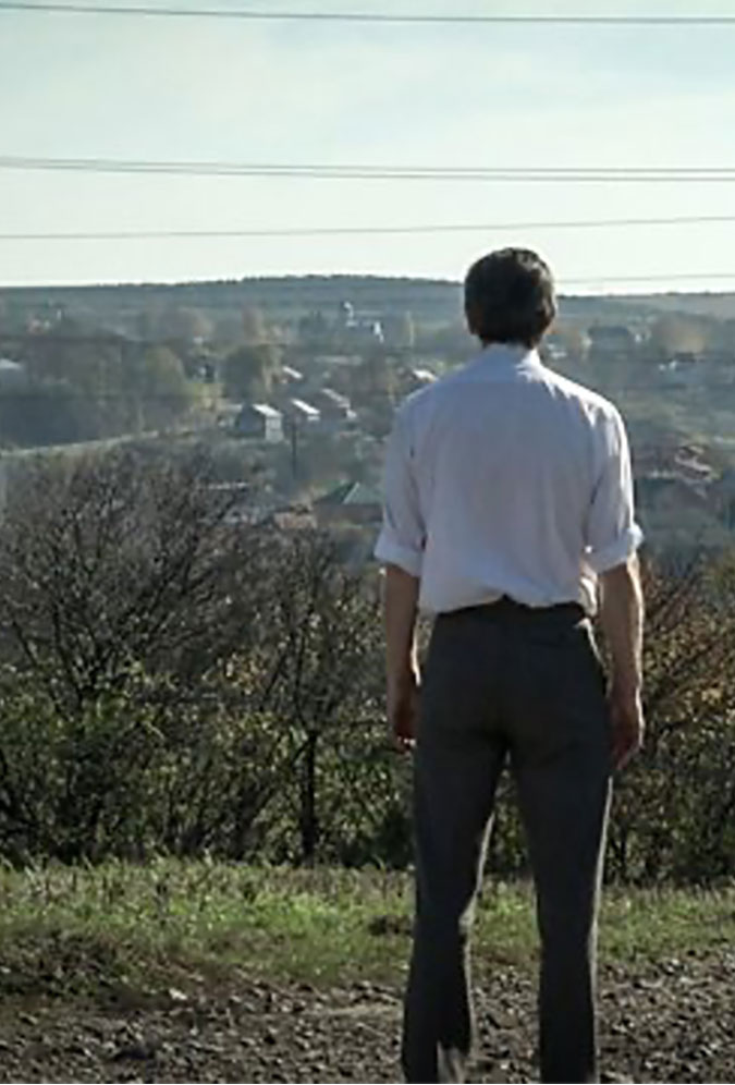 Still image from Circling a Fox. A man stands with his back to the camera looking at a landscape with houses