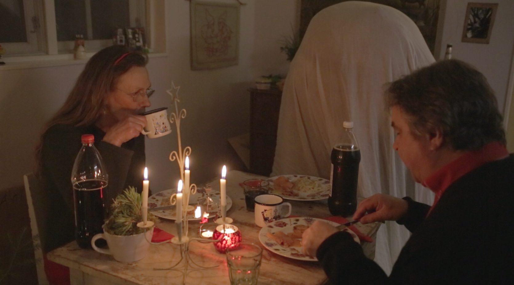 Dinner table with man and woman and un seen person draped in white sheet.