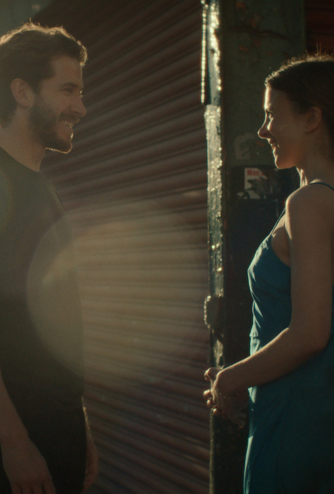 Still from Falling into Place. Man and woman converse on quiet street with the sun low in the sky.