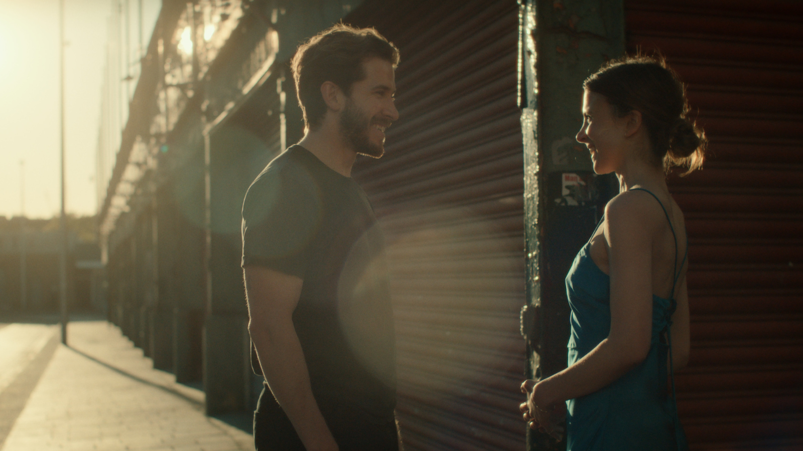 Still from Falling into Place. Man and woman converse on quiet street with the sun low in the sky.