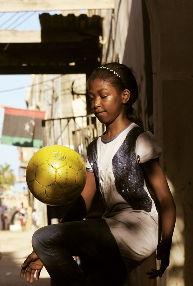 Freedom Fields Poster. A young black girl knees a bright ball