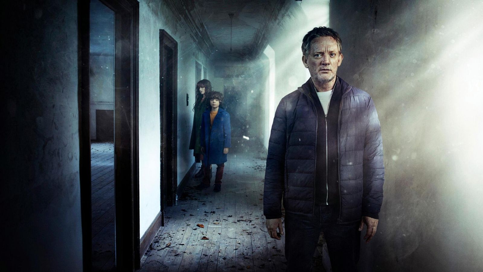 Douglas Henshall stands in a spooky hallway, with a woman and her son in the background