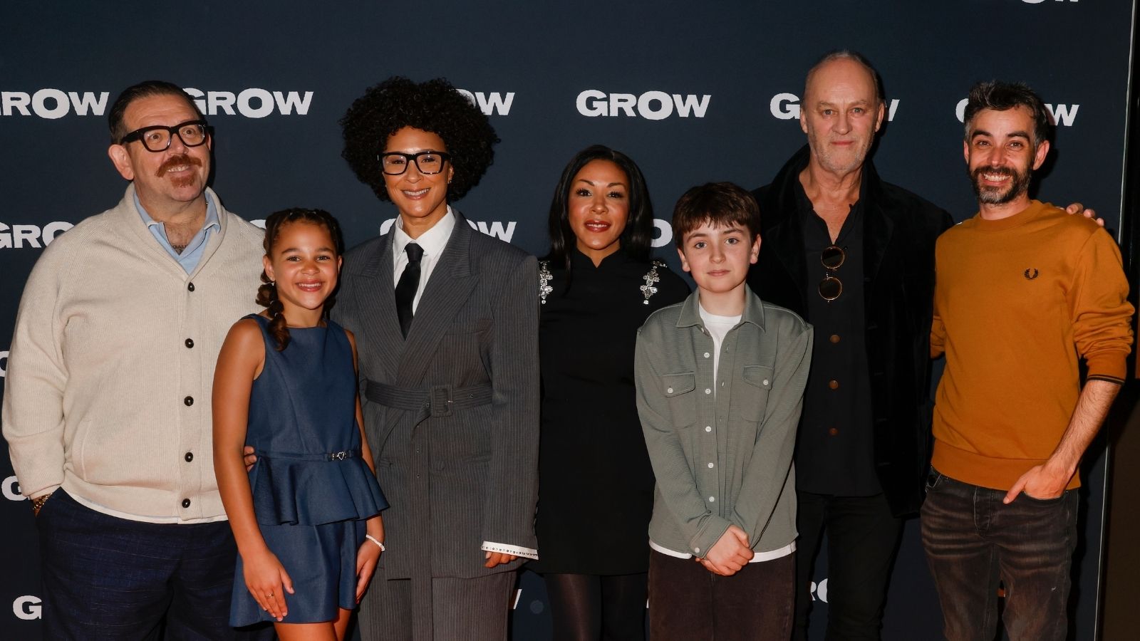 Seven people stand together in front of a dark backdrop with the word 