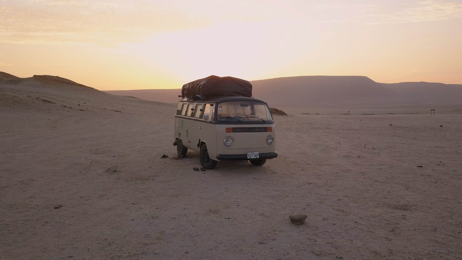 A dusty beaten up campervan in a desert at sunset. Still from La Sagrada Familia.