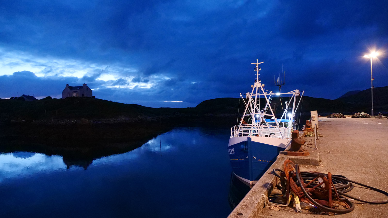 Still image from iorram (Boat Song) showing a boat in a harbour at night