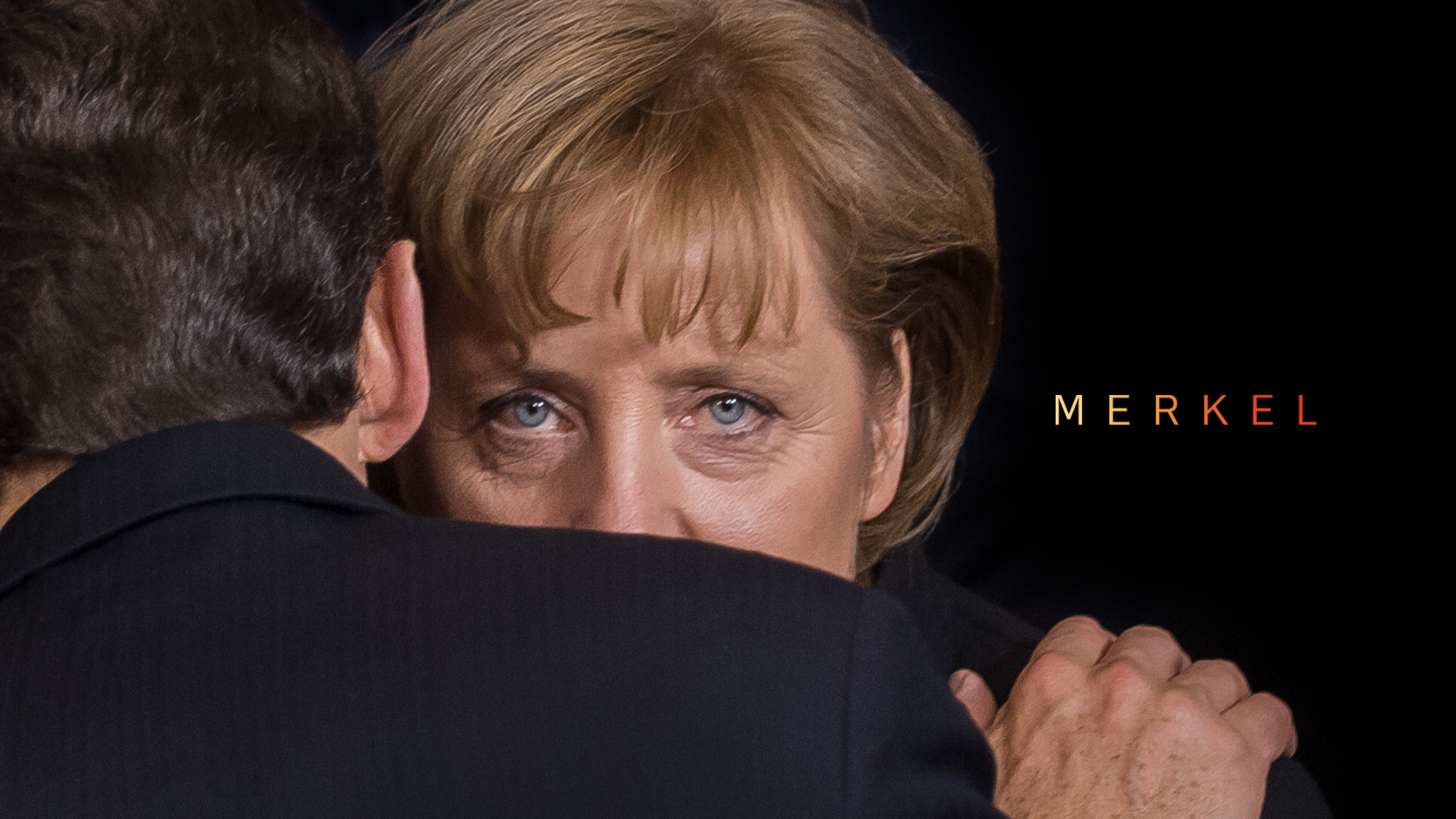Angel Merkel slooking over a man's shoulder staring directly at camera.