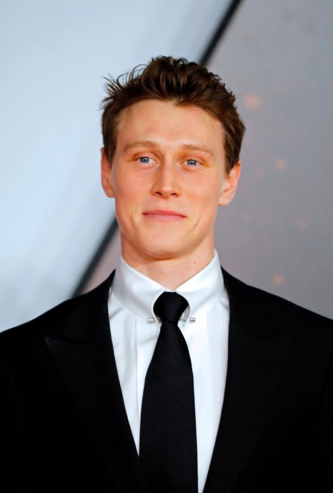 Headshot of actor George MacKay, who wears a black suit and tie, and a white shirt. Photo by TOLGA AKMEN/AFP via Getty Images