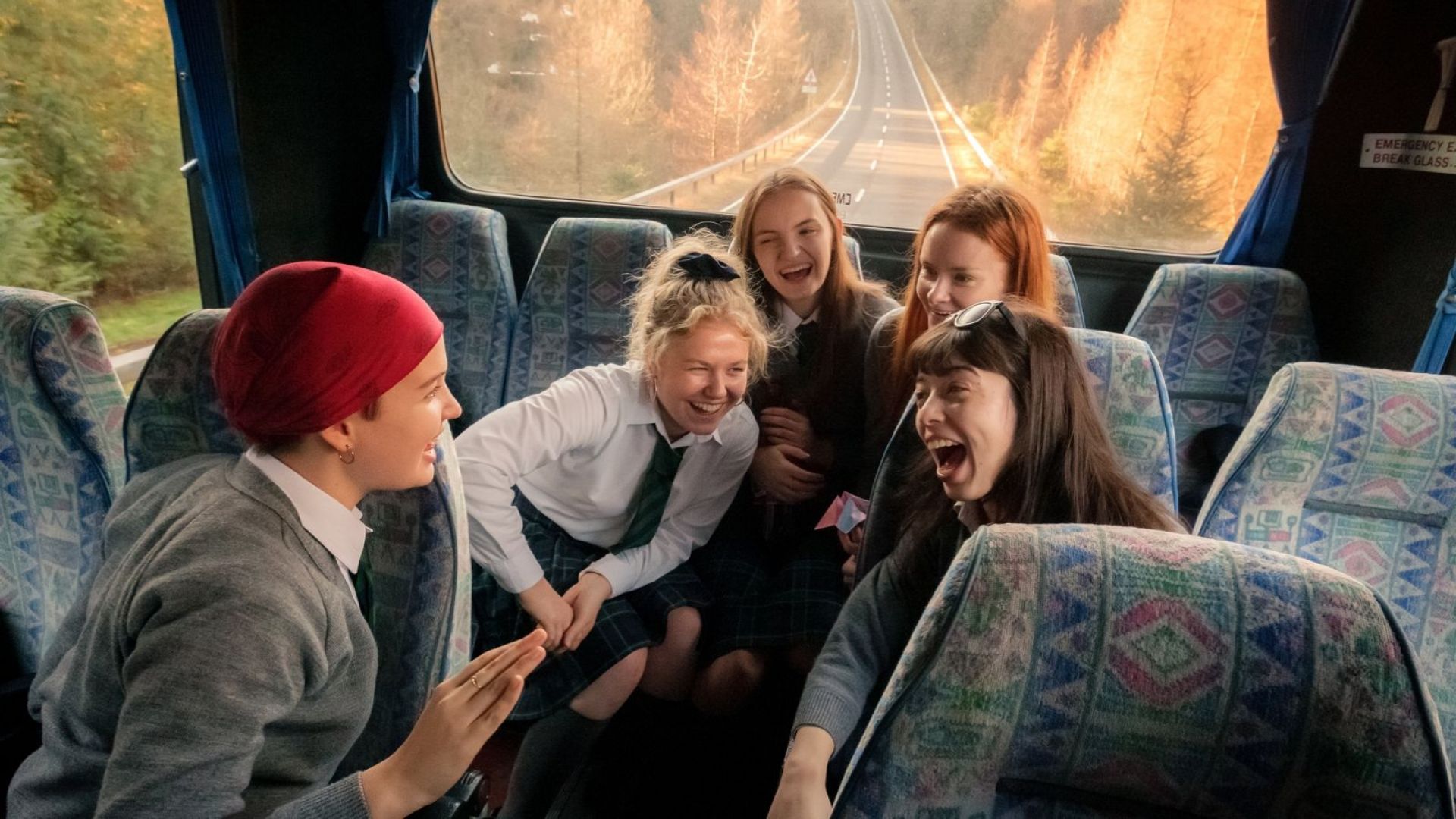 A group of girls sit laughing at the back of the bus