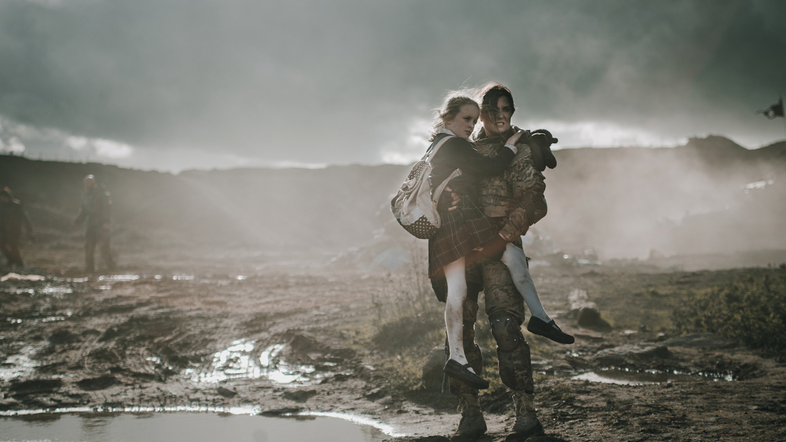 A soldier holds a young girl, looking out onto battle