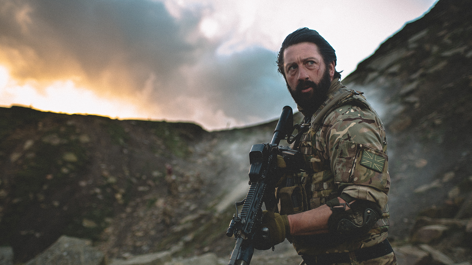 An armed soldier looks alert on a landscape