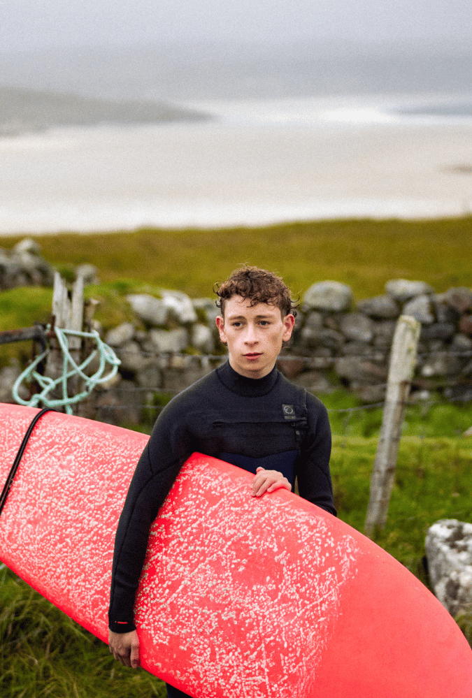 Still from silent Roar. Teenage boy in wetsuit holding red surf board.