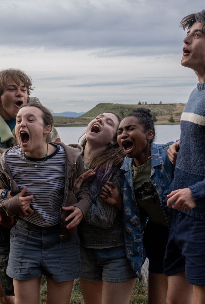 Image shows five young people standing on the shore of a loch shouting excitedly