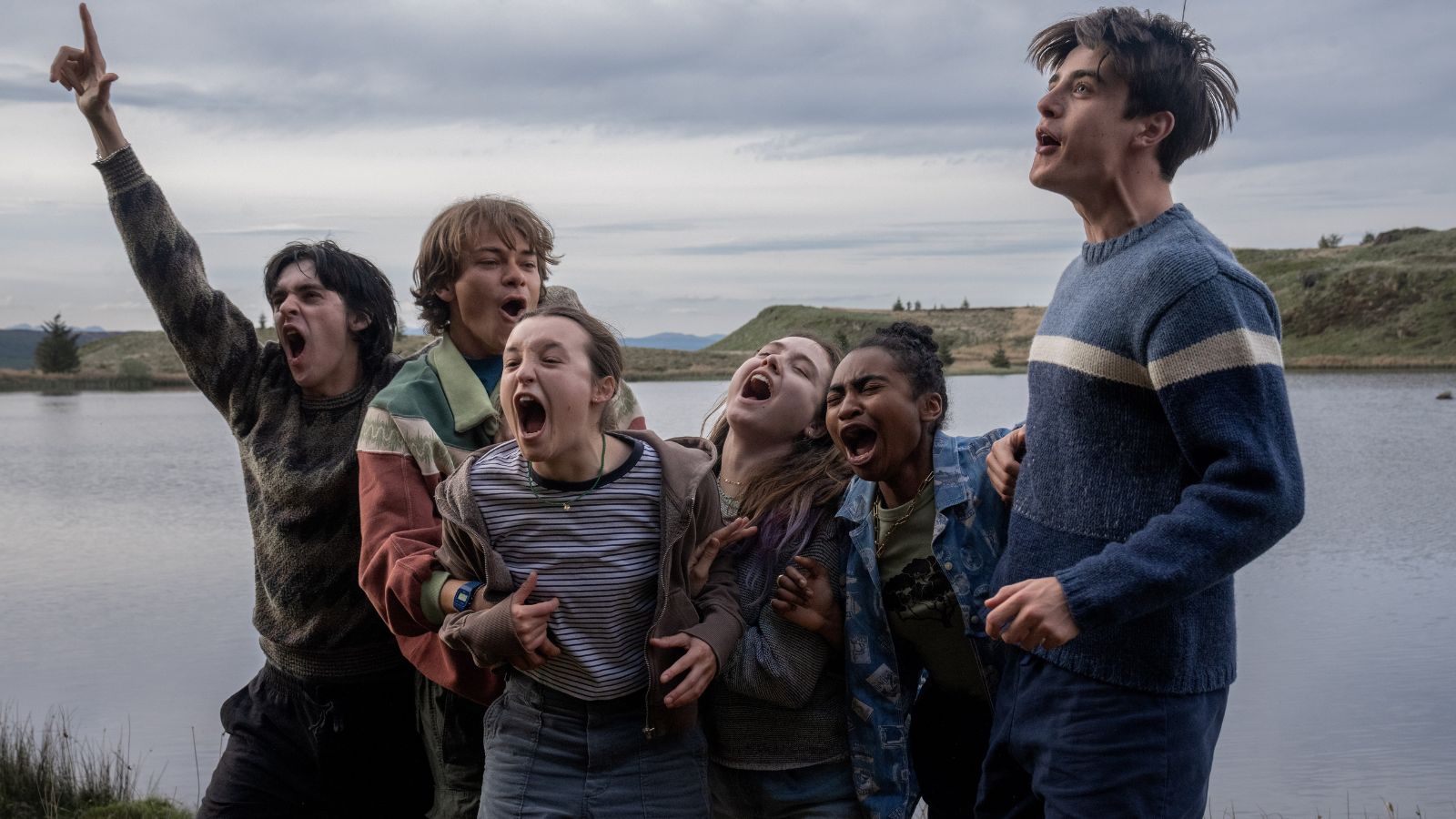 Image shows six young people standing on the shore of a loch shouting excitedly