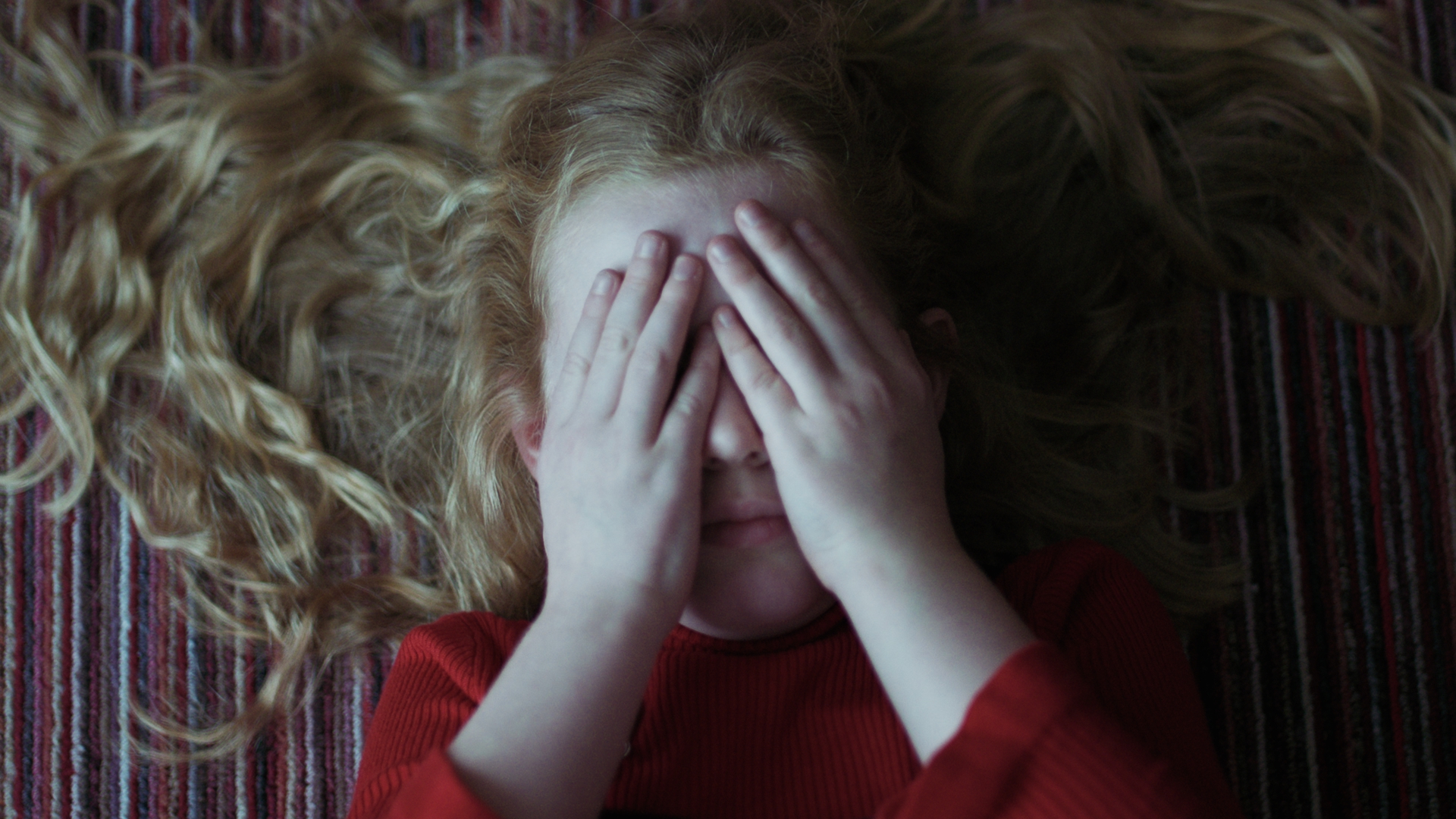 Woman lying down with hands covering her face.