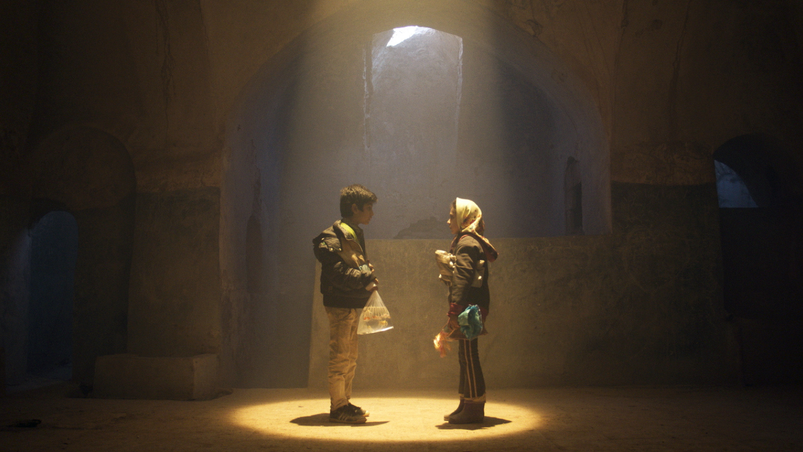 A Still from Hamam. A young boy (Yahya) and a young girl (Leila) stand facing each other, illuminated by a bright white spotlight