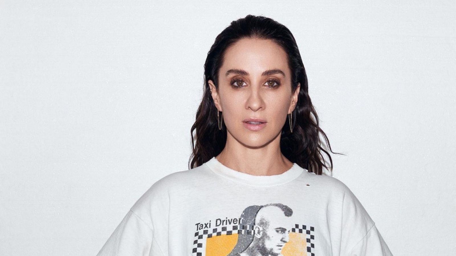 A person with dark hair wearing a white T-shirt featuring a graphic of a man with a mohawk and the phrase 