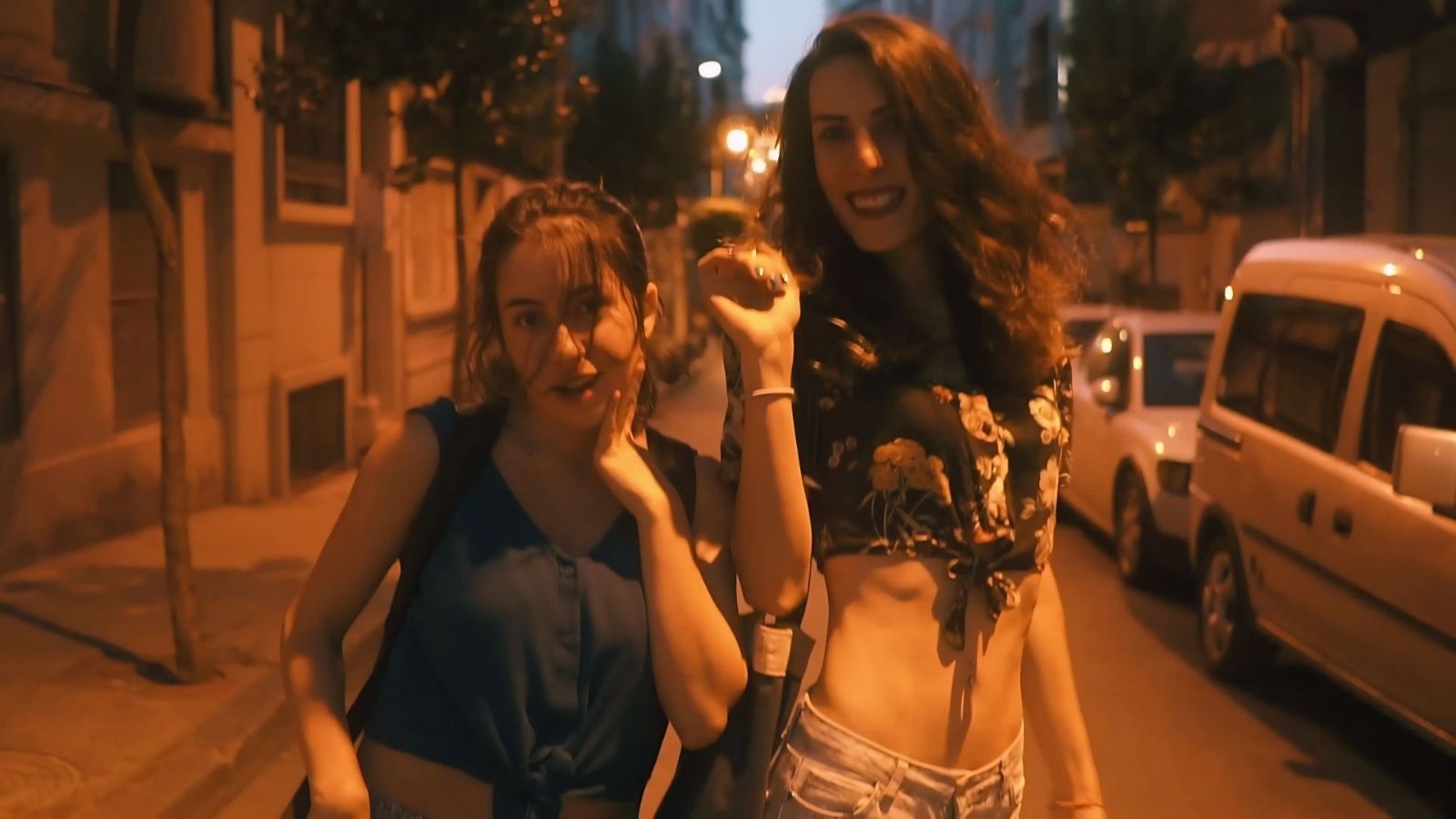 Two people walk down a street in the evening, laughing