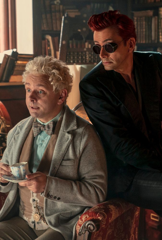 The characters of Aziraphale and Crowley from Good Omens sit in a living room drinking cups of tea