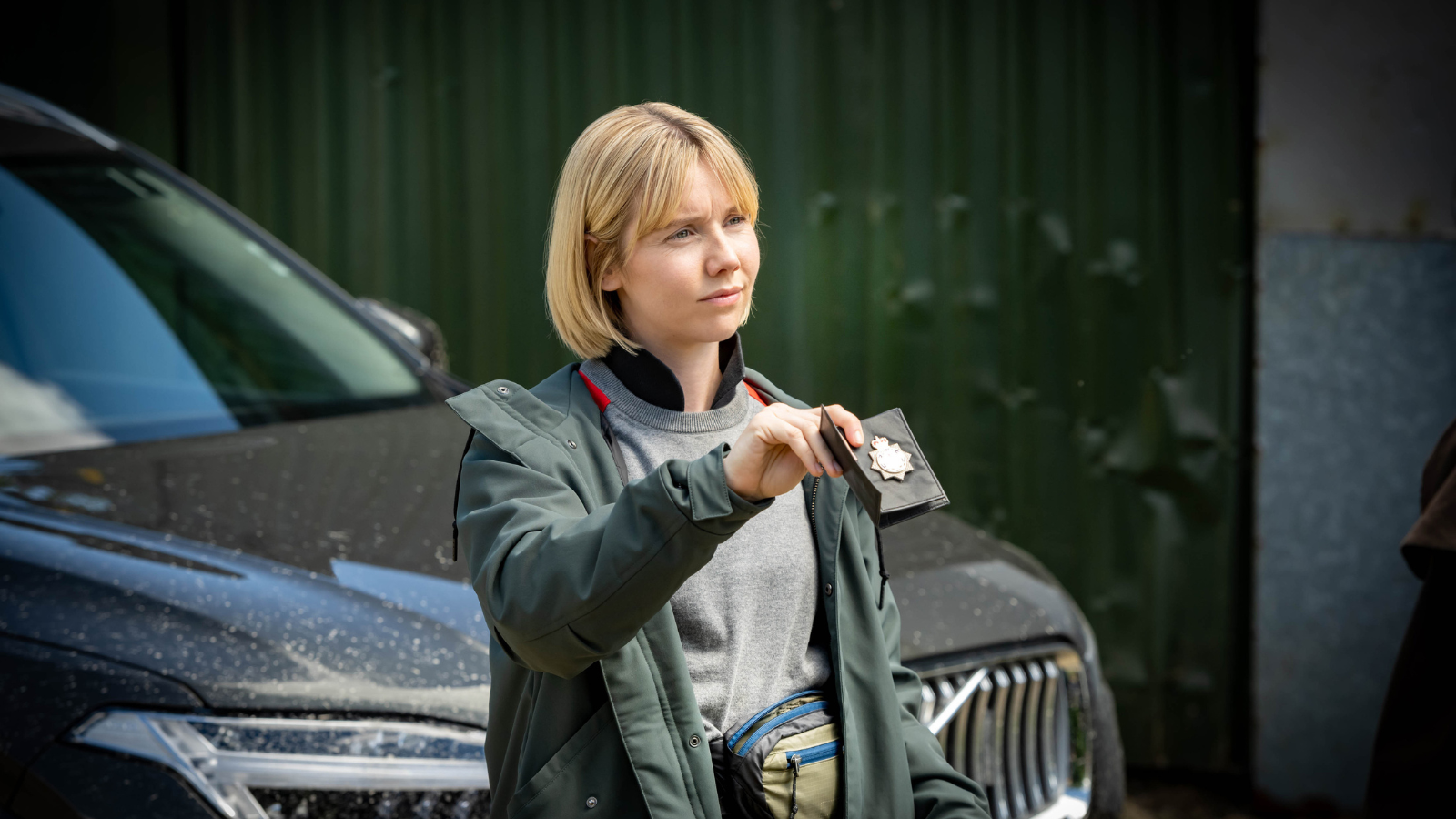 Karen Pirrie holding her police badge standing in front of a car