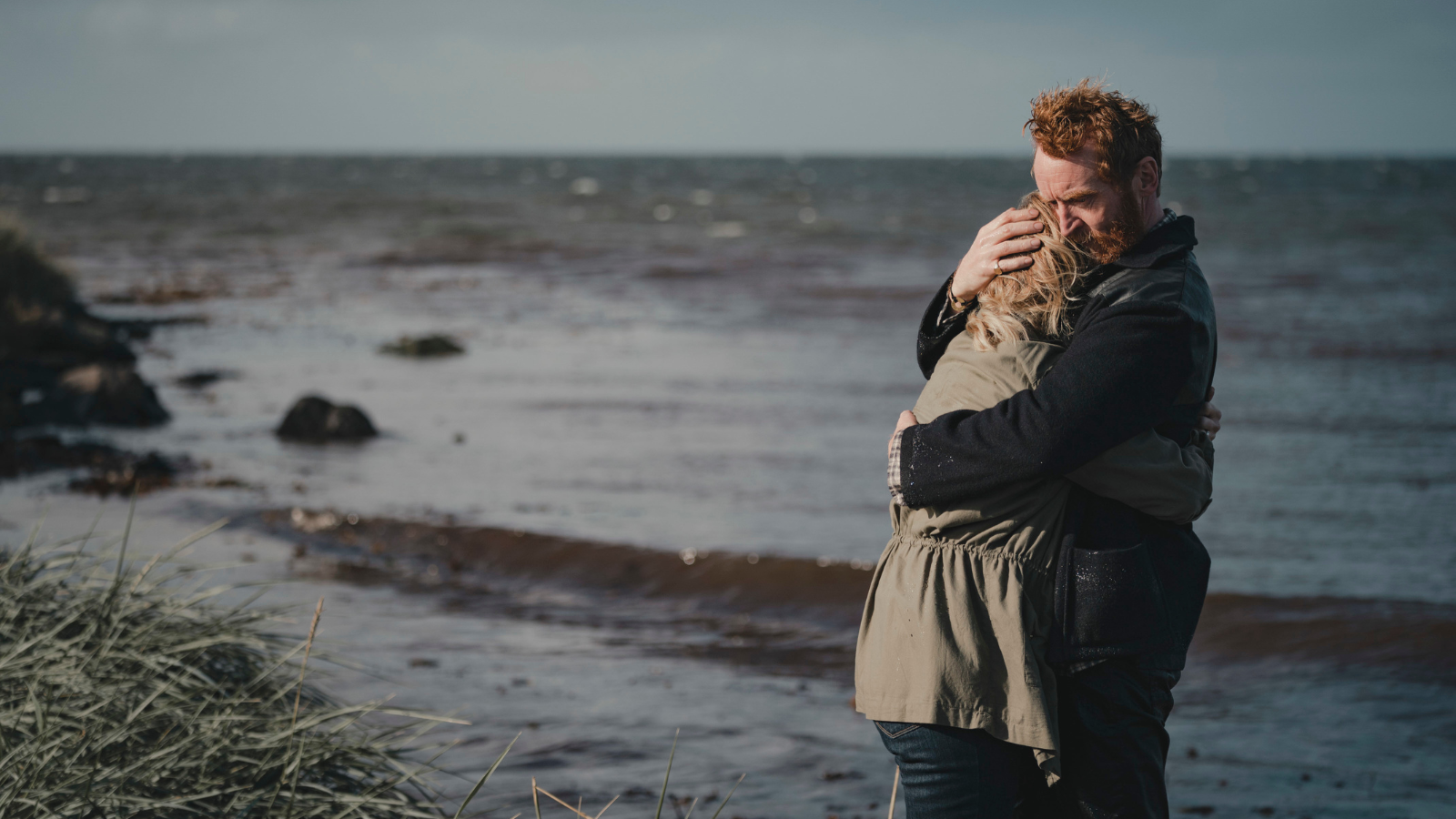 Still from Mayflies. Tony Curran and Ashley Jensen hug on a beach.