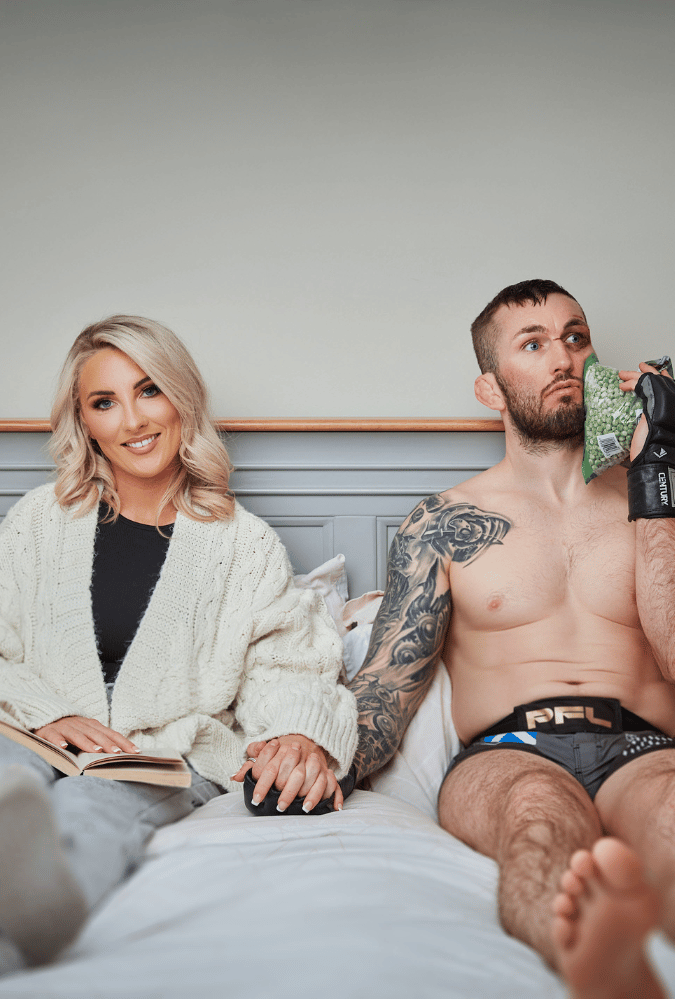 Natalie and her MMA husband Stevie Ray lying on their bed. Natalie wears a dressing gown while Stevie is topless in MMA boxers holding an ice pack to his face.