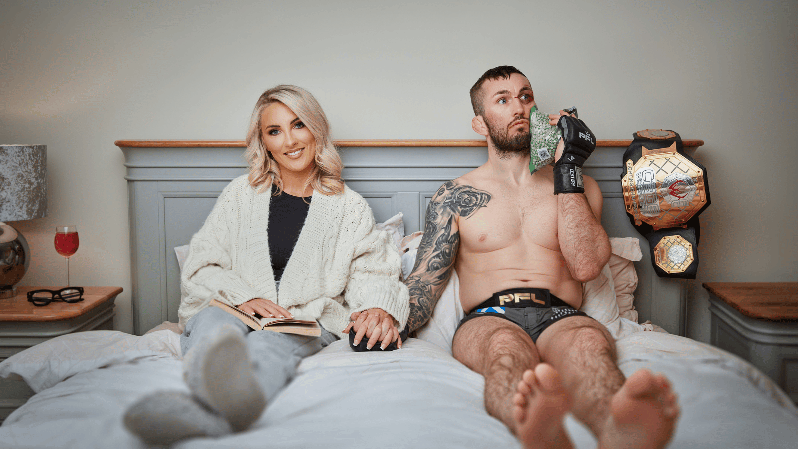 Natalie and her MMA husband Stevie Ray lying on their bed. Natalie wears a dressing gown while Stevie is topless in MMA boxers holding an ice pack to his face.