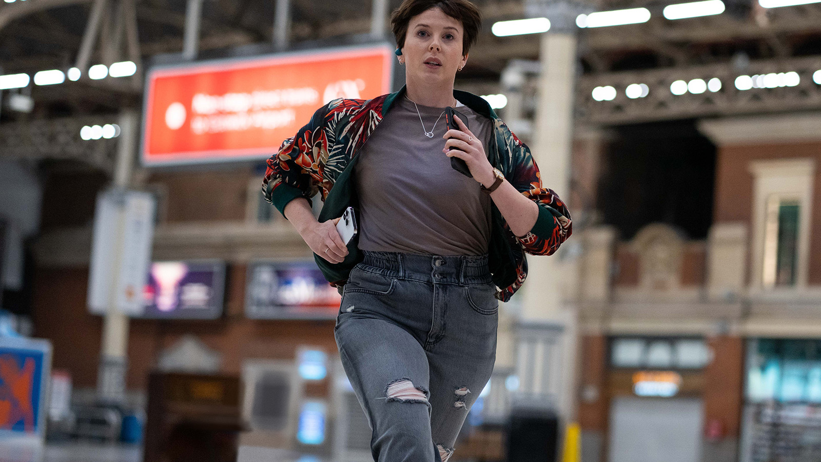 Alexandra Roach as Abby Aysgarth. She is holding two mobile phones and runs through a train station looking panicked.