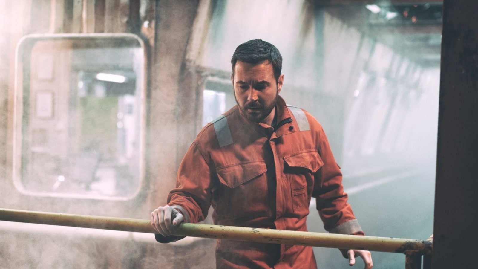 Mark Compston plays a rig worker - he stands in an orange boilersuit looking down over a railing