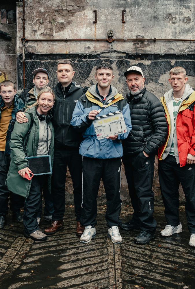 The cast and director and producer of The Young Team stand in a row - the cast are all wearing various styles of tracksuit