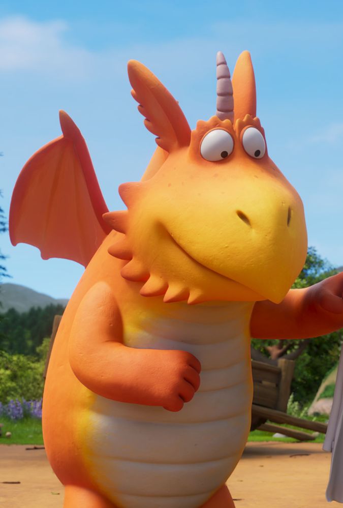 An orange cartoon dragon with a single horn and wide eyes stands outdoors on a sunny day, with green trees and blue sky in the background.