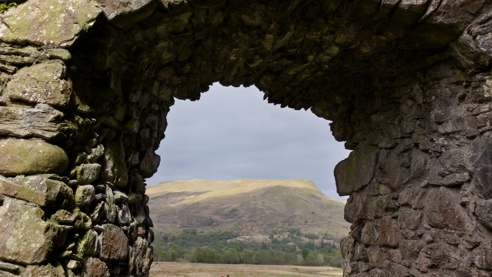 A view of green landscape, through a stone archway situated in Kilchurn Castle
