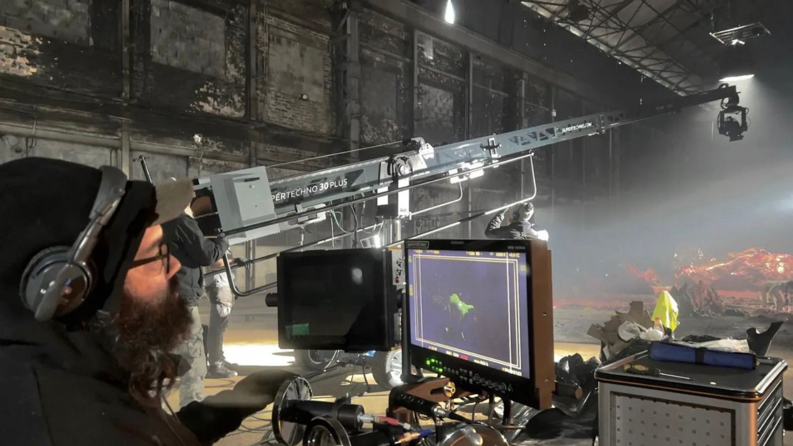 Man on film set looking into monitor. There is a large camera crane capturing a scene taking place further down in the film studio.