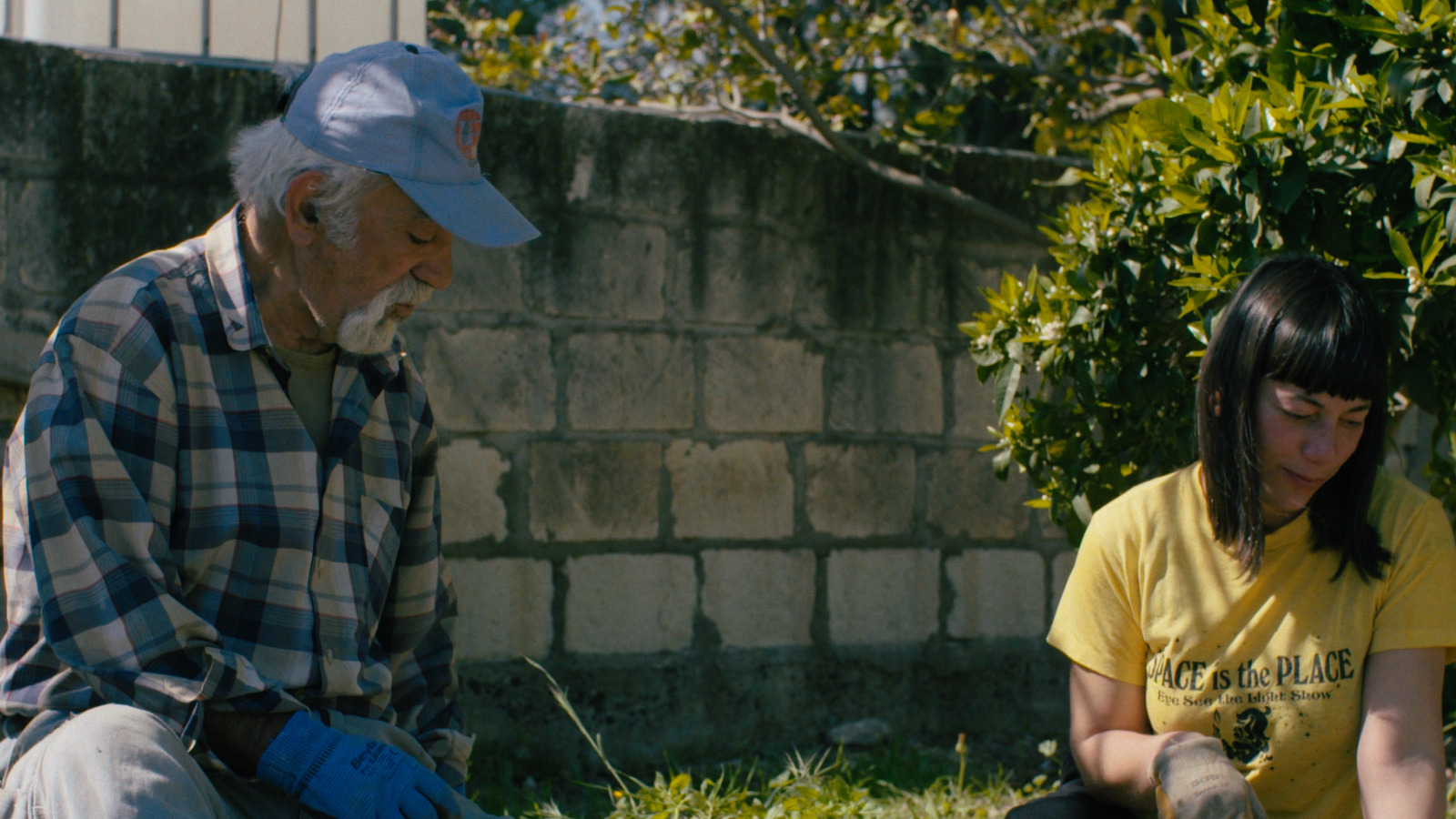 Still from Pembe Ay. Woman sits outsides on a sunny say gardening with an older man kneeling next to her.