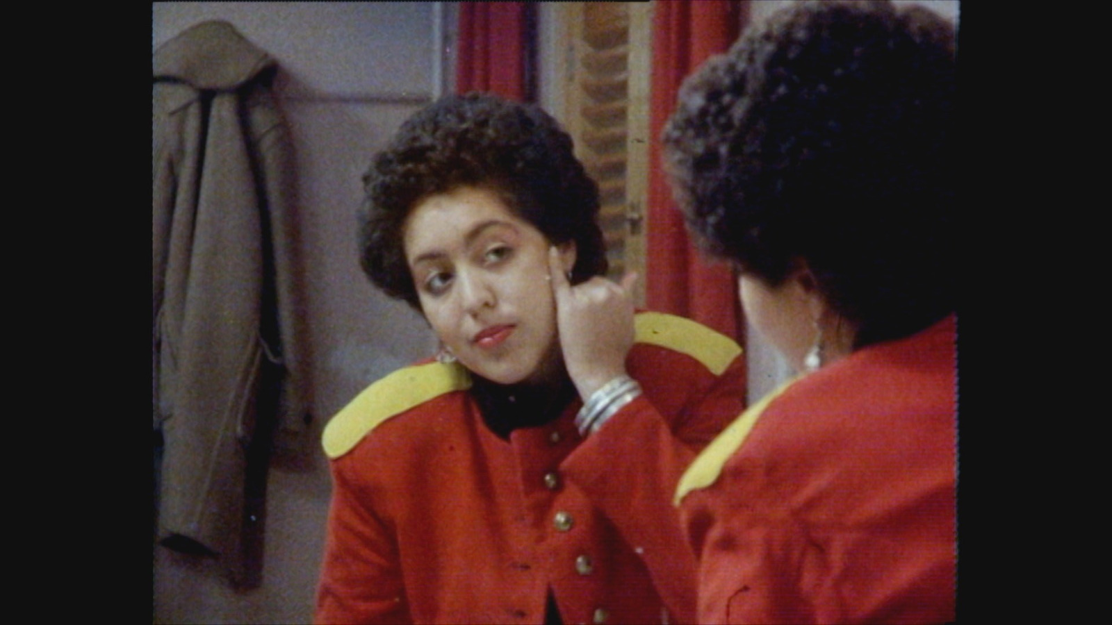 Poly Styrene in red army jacket putting on make up in the mirror.