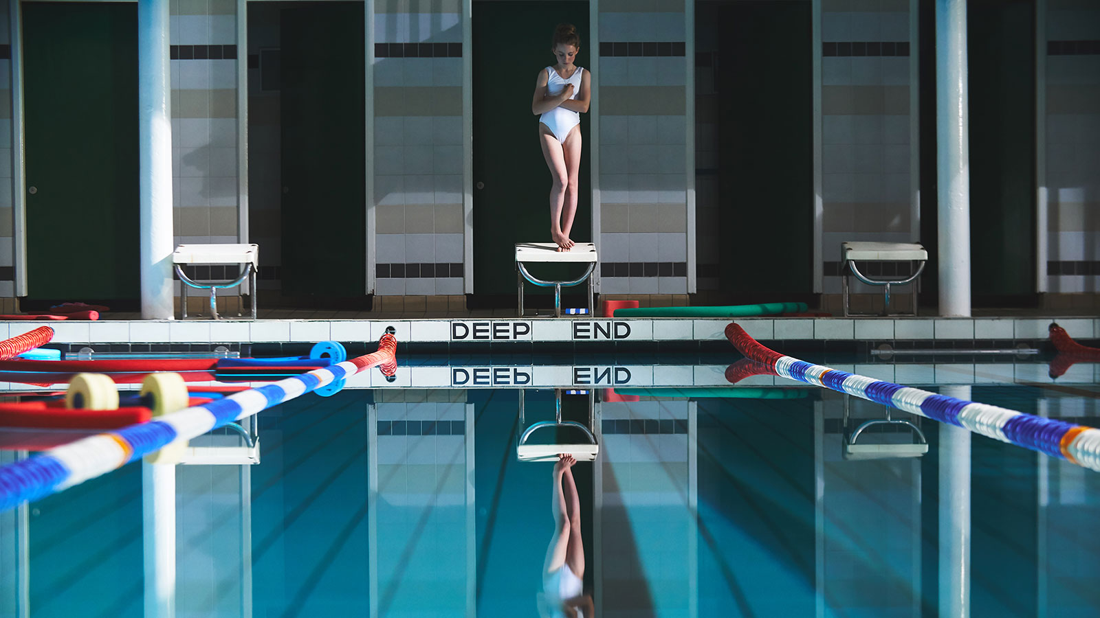 A young girl stands on a diving board about to jump into a pool