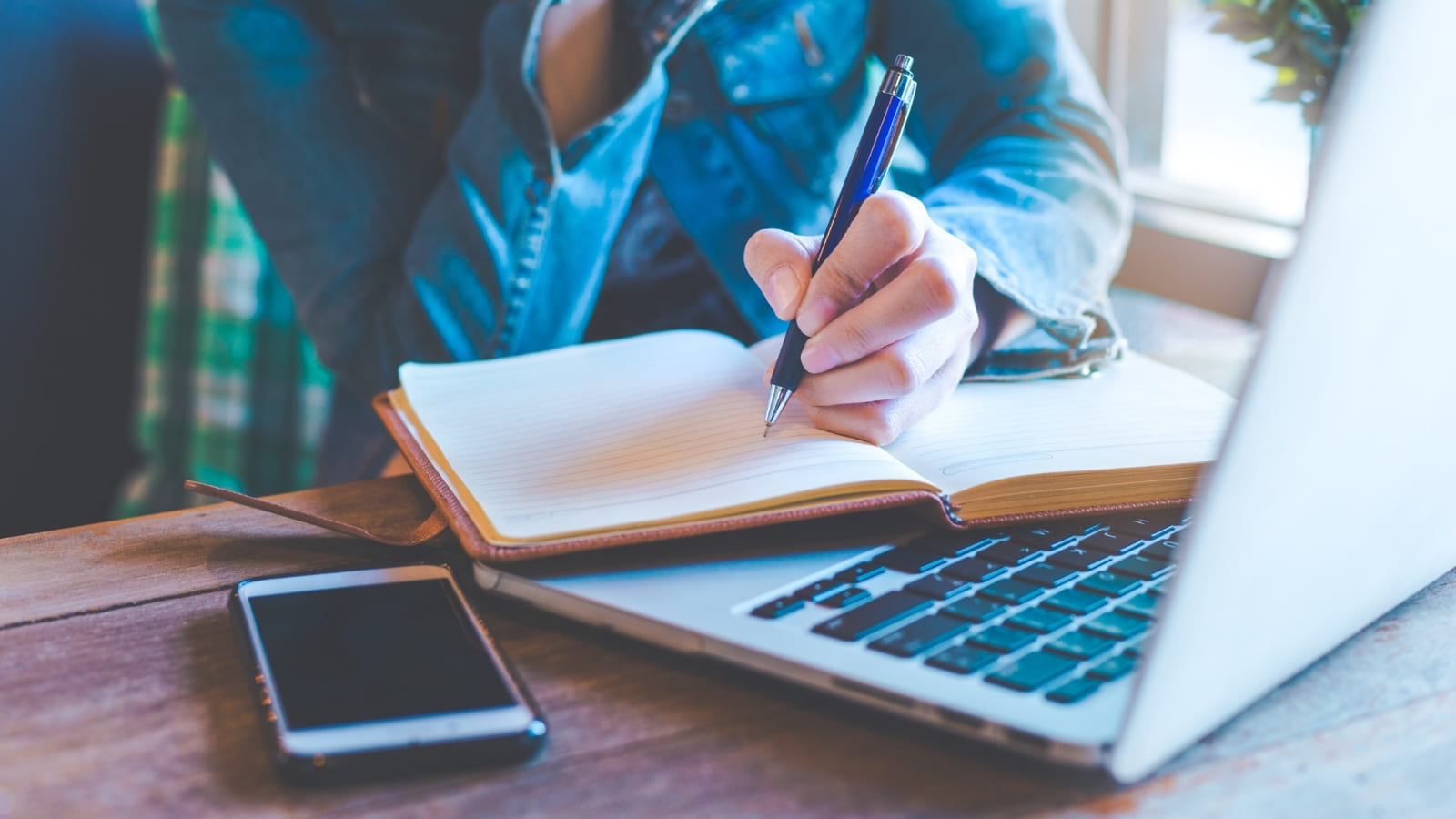 A person sits at a desk writing in an open notebook