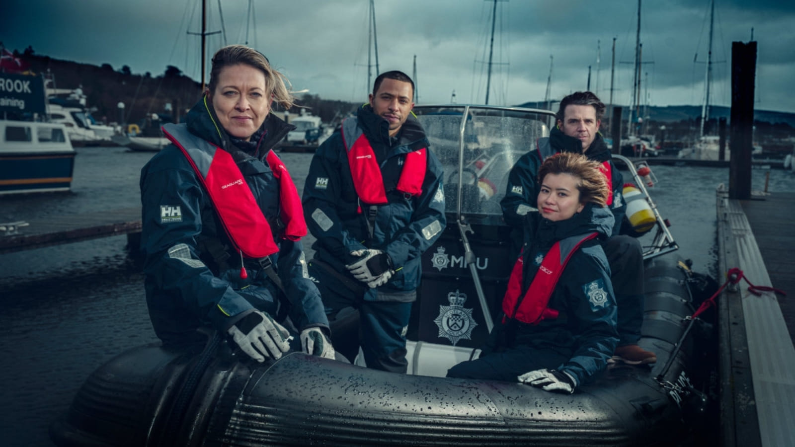 The cast of Annika sit together on a boat under a stormy sky