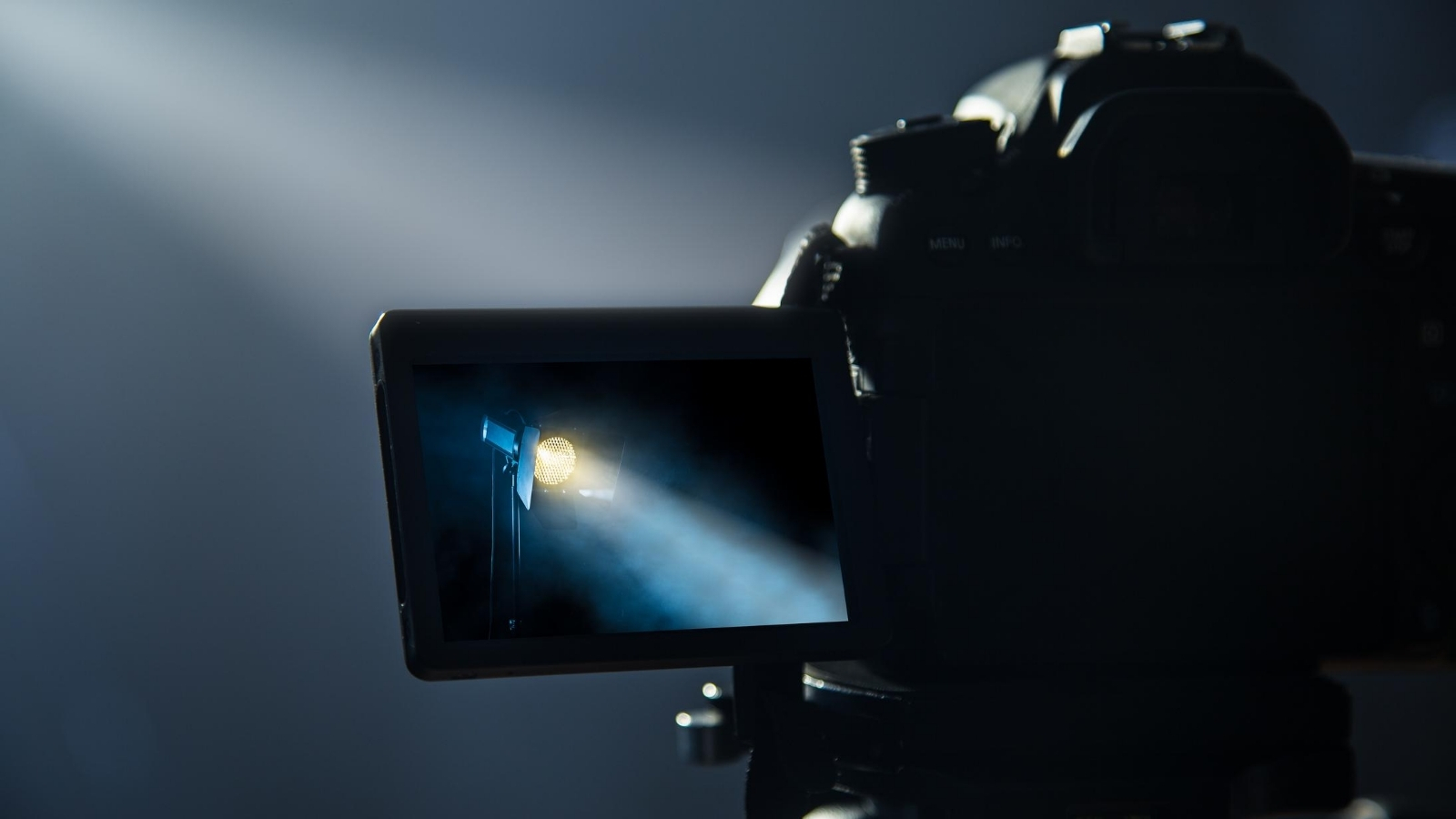 A close up, dramatic shot of a high quality film camera. On the camera's screen you can see a close up of a spotlight. The background is dark and misty