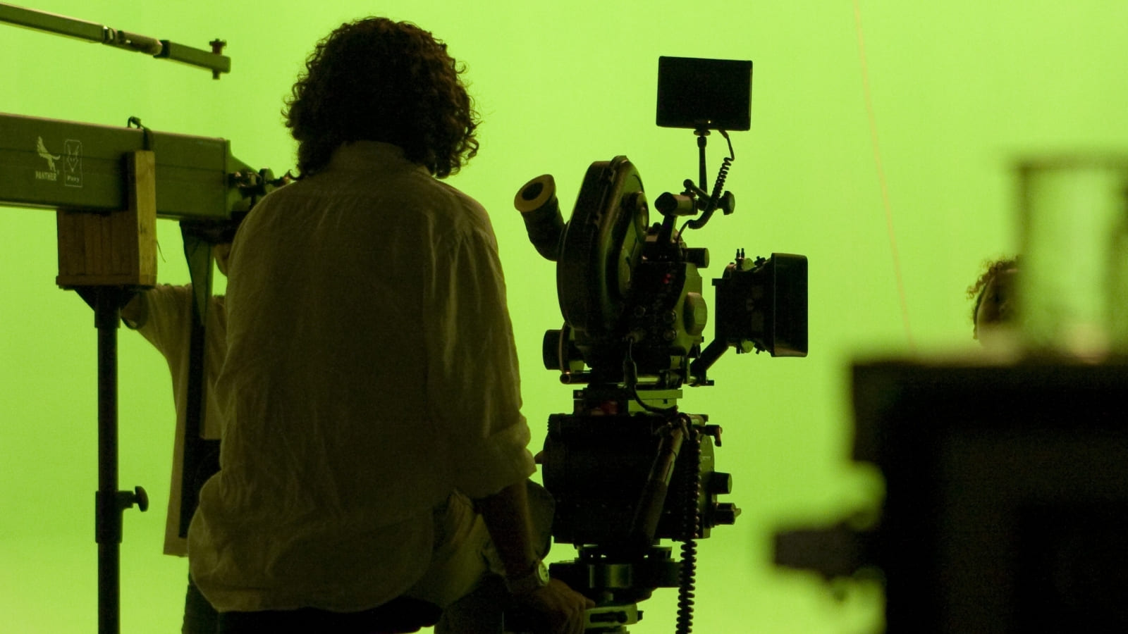 A camera operator sits in a green screen studio with a film camera set up